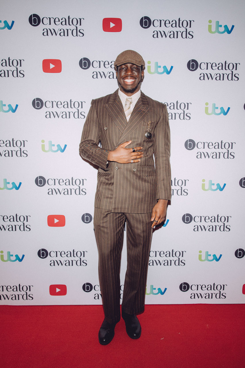 Your Boy Moyo vintage/Peaky Blinders look pin striped suit with flat cap and pocket watch on red carpet